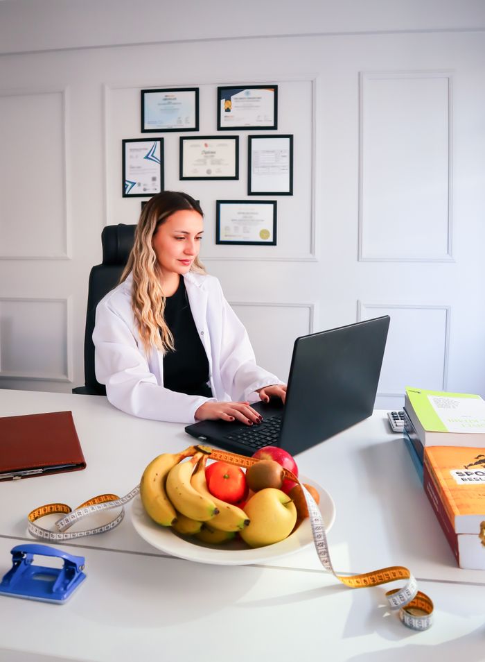 Nutritionist working at desk with laptop and healthy fruits in office setting.